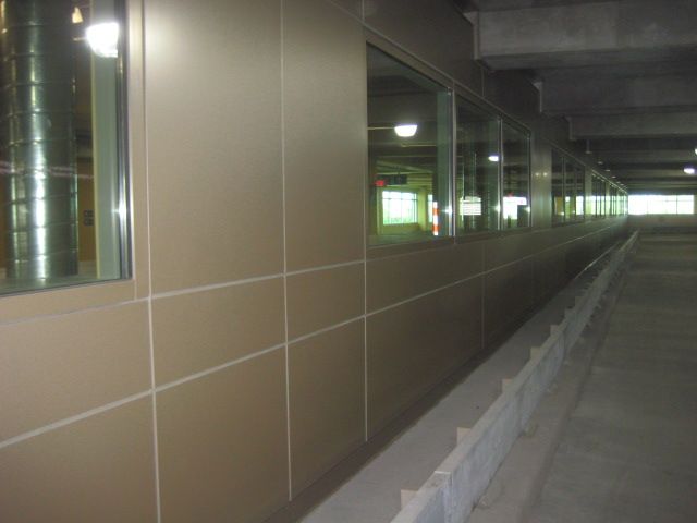 Tan wall with windows and a concrete ramp in a parking structure.
