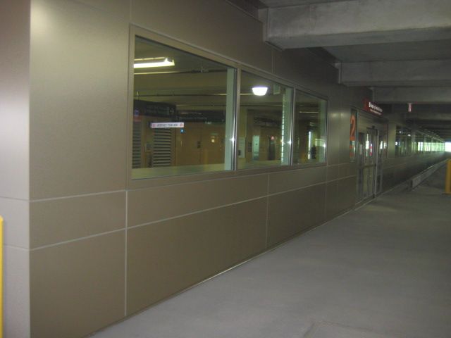 A long, beige-paneled hallway with windows, likely in a parking garage. Concrete floor and ceiling.