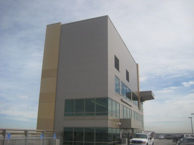 Three-story beige and tan building with large windows and a small overhang, cloudy sky in the background.