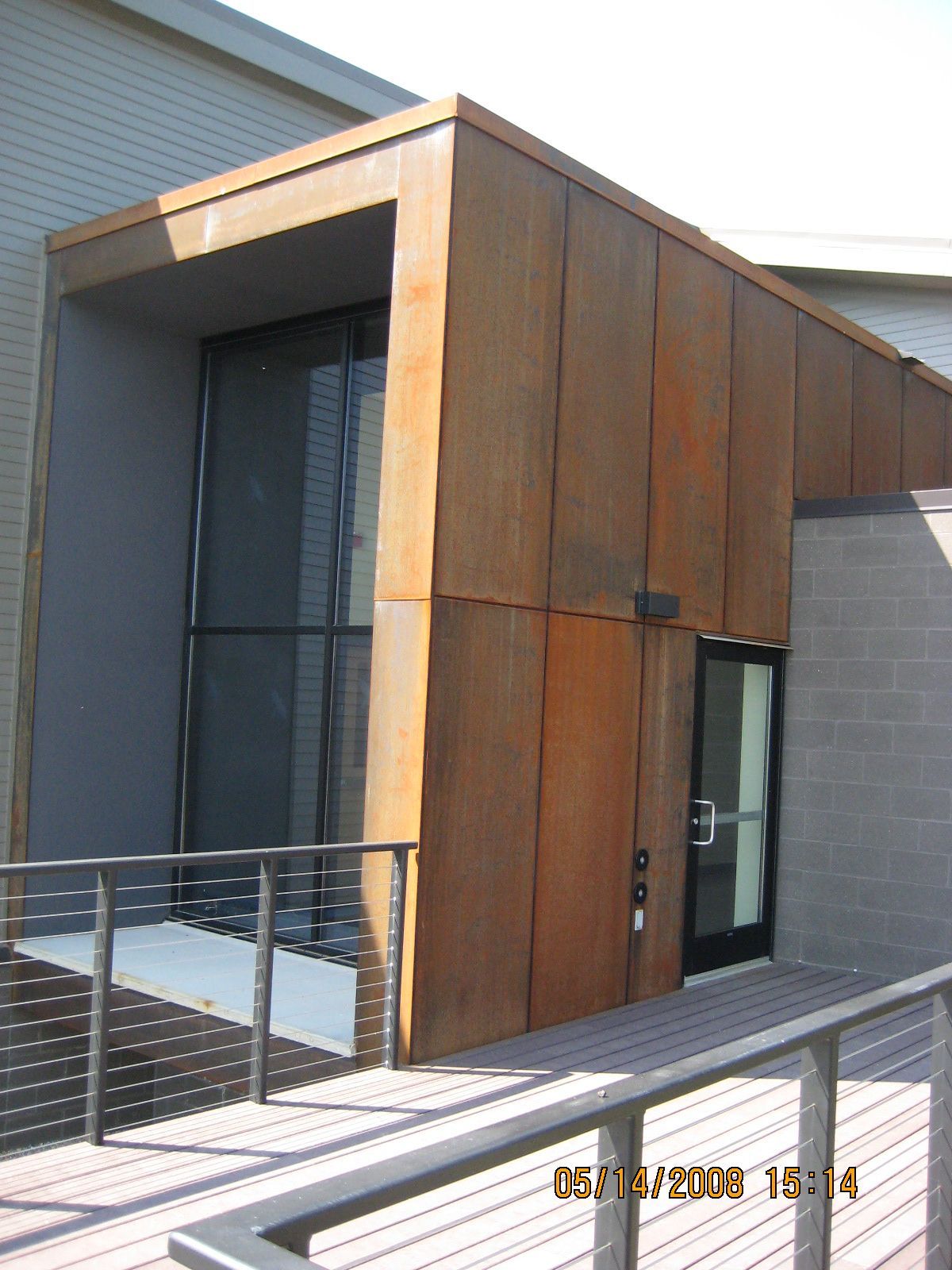 Exterior entrance with weathered brown panels, glass door and window, and a ramp with railing.