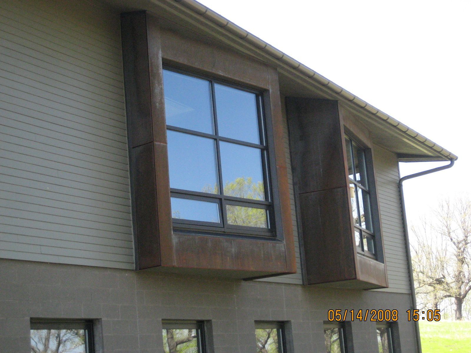 Two windows with weathered-metal frames on a building with light siding.