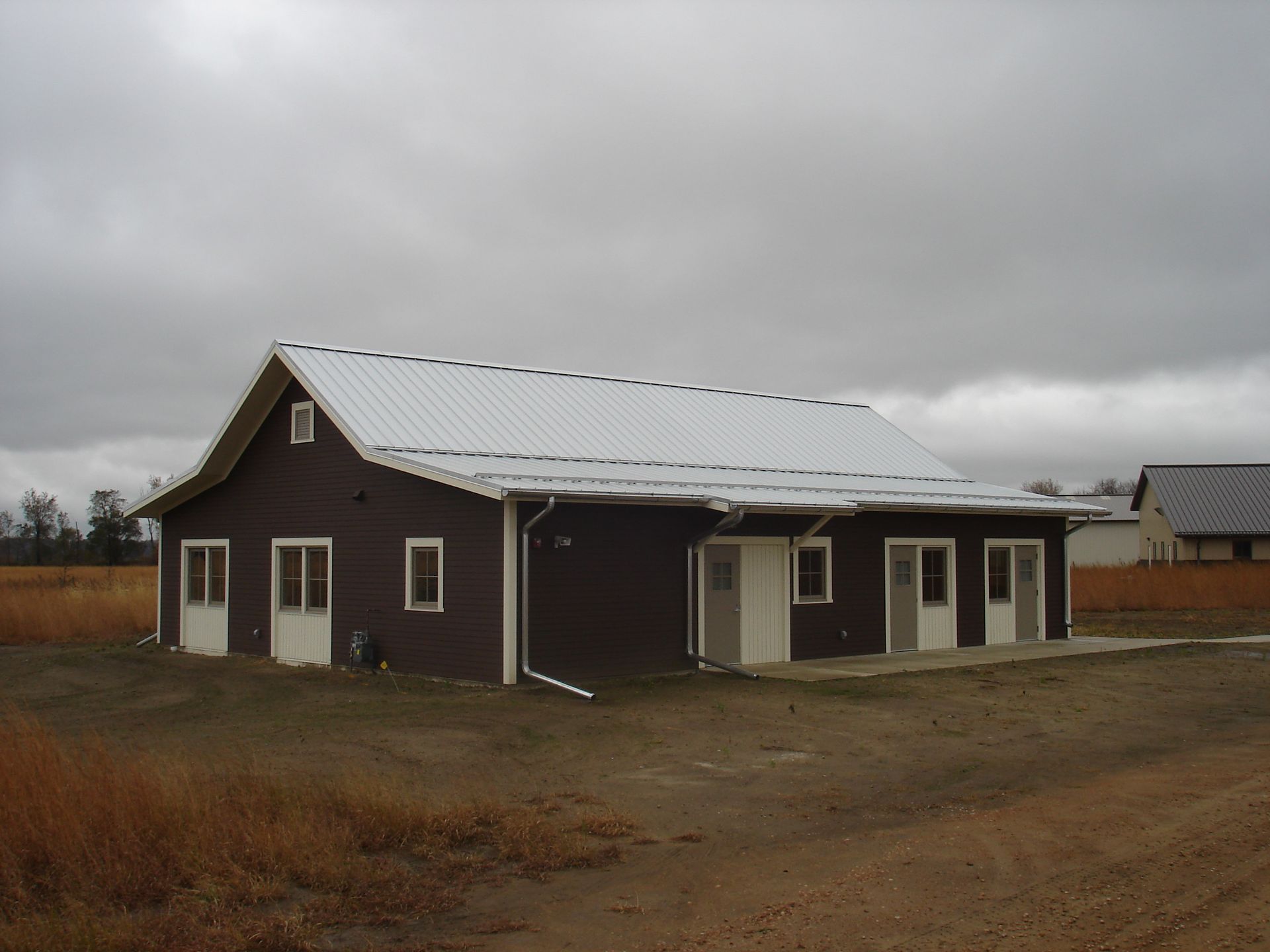 Brown building with white trim and metal roof under cloudy sky.