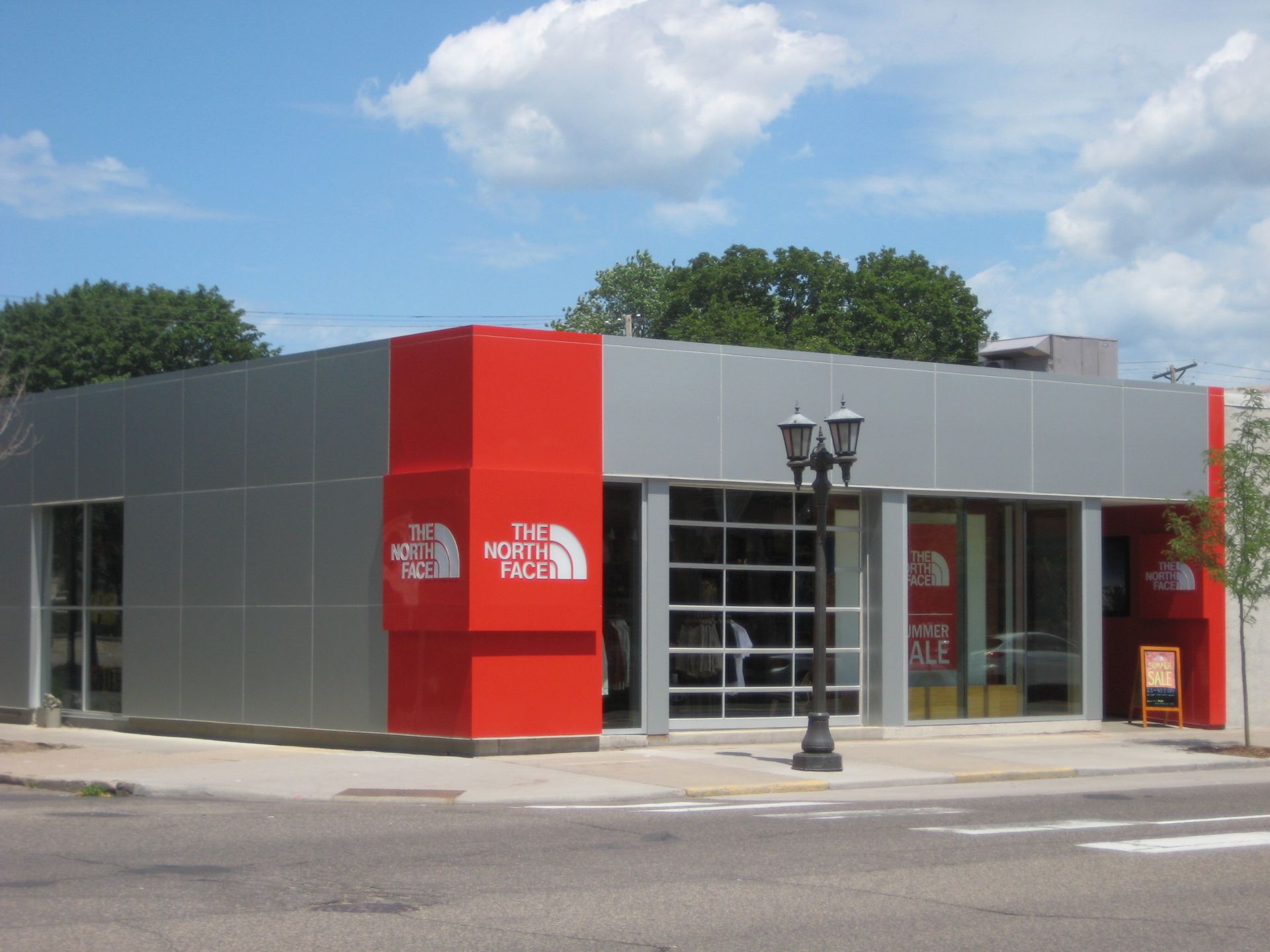 The North Face store, gray and red exterior, glass storefront, cloudy sky.