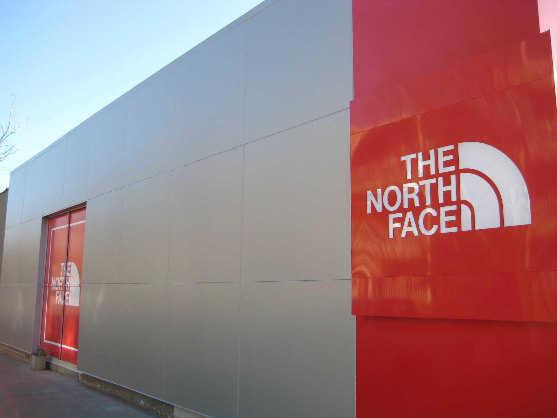A red and silver The North Face store with its logo displayed prominently on a red pillar.