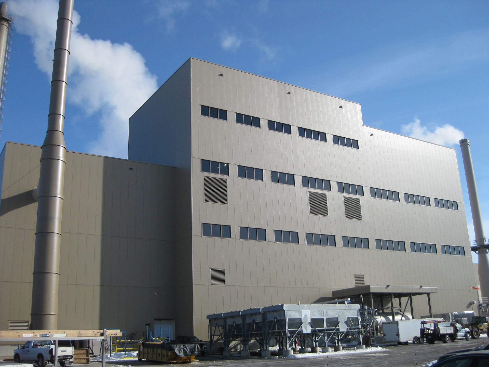 Large beige industrial building with smokestacks against a blue sky, possibly a power plant.