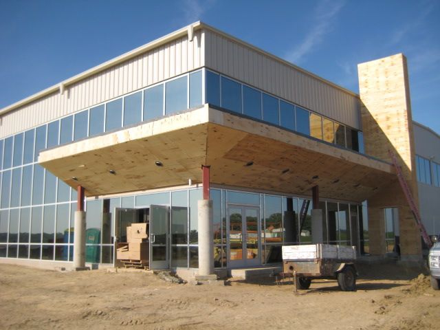 Building under construction with glass windows and a concrete overhang. Metal siding and a clear sky.