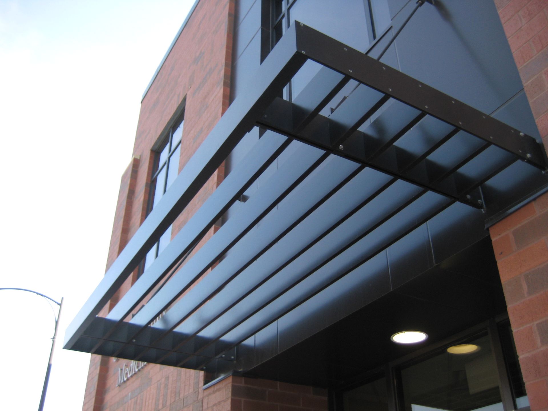 Black metal awning over a building entrance with brick and dark facade.