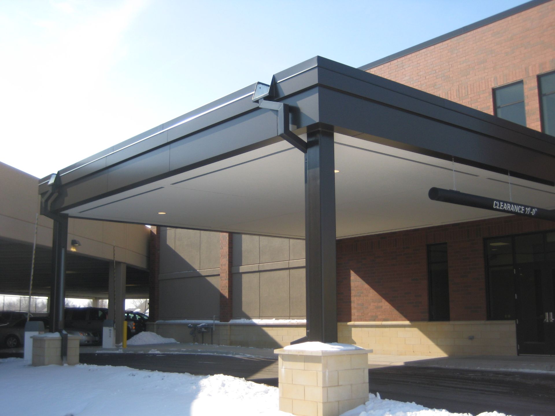 Black canopy over building entrance with support columns and a light-colored soffit; snow in the foreground.