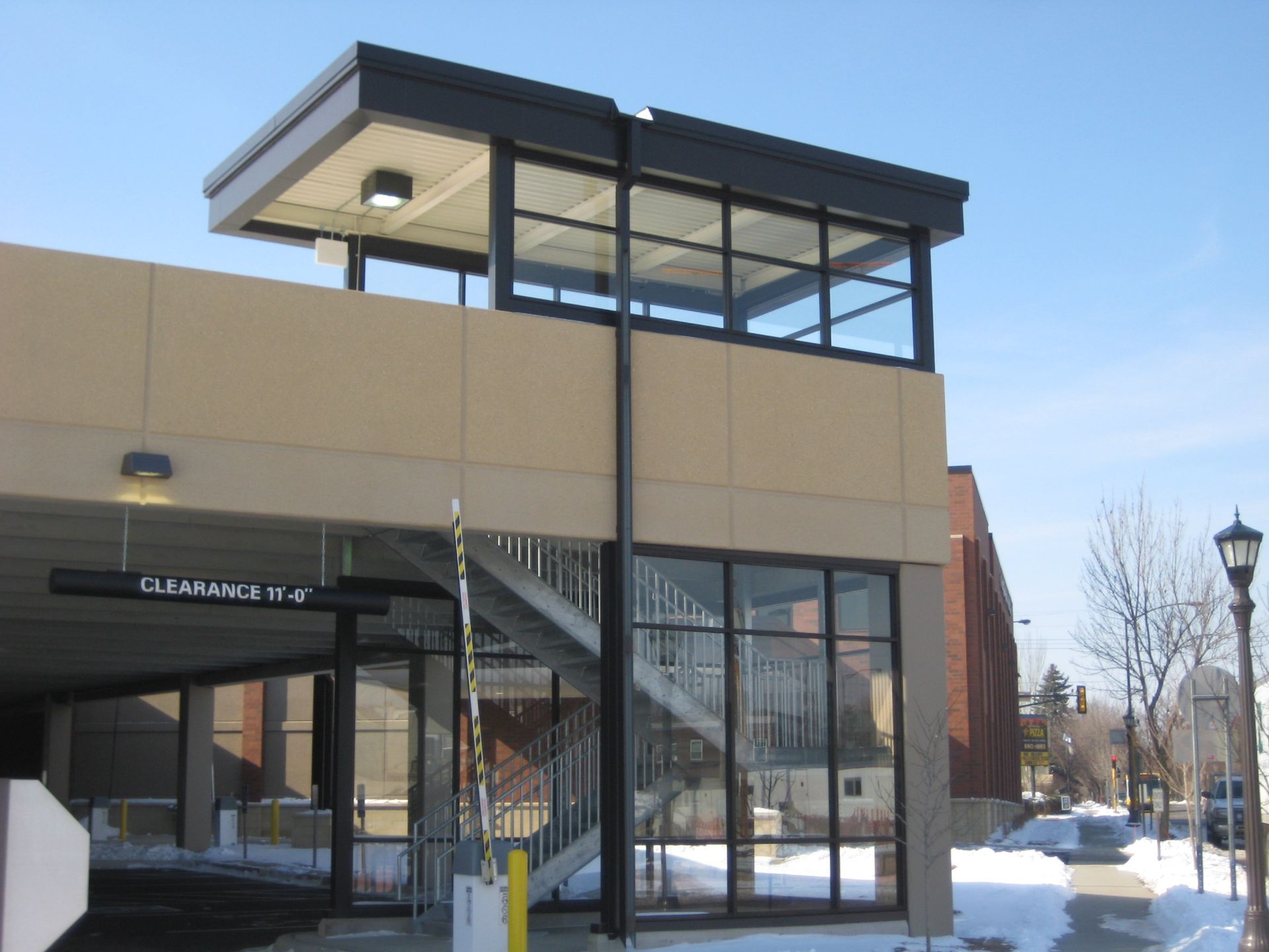 Exterior of a parking garage exit with a glass enclosed stairwell and a clearance sign.