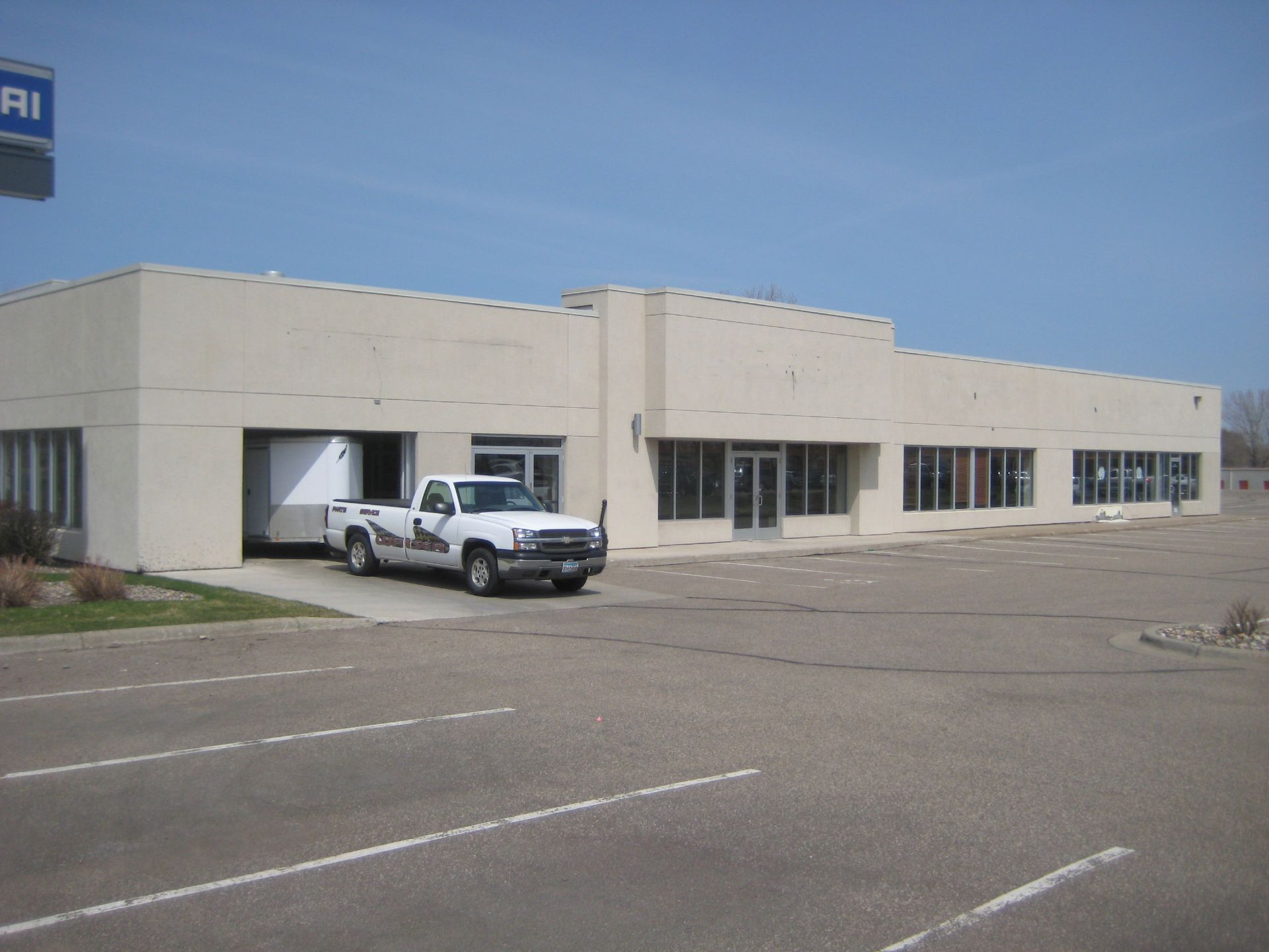 Beige building with a white truck parked in front. Blue sign visible.