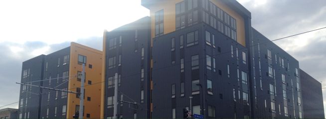 A multi-story building with dark siding and orange accents under a cloudy sky.