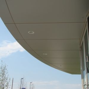Curving, light-colored building exterior with recessed lights, against a partly cloudy blue sky.
