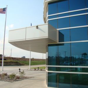 Modern building with curved glass facade, overhang, and American flag on a sunny day.