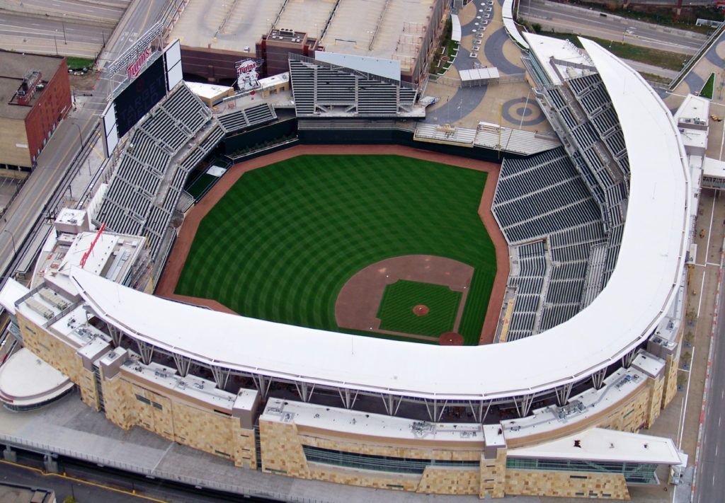 Aerial view of a baseball stadium with a green field, seating, and a curved white roof.