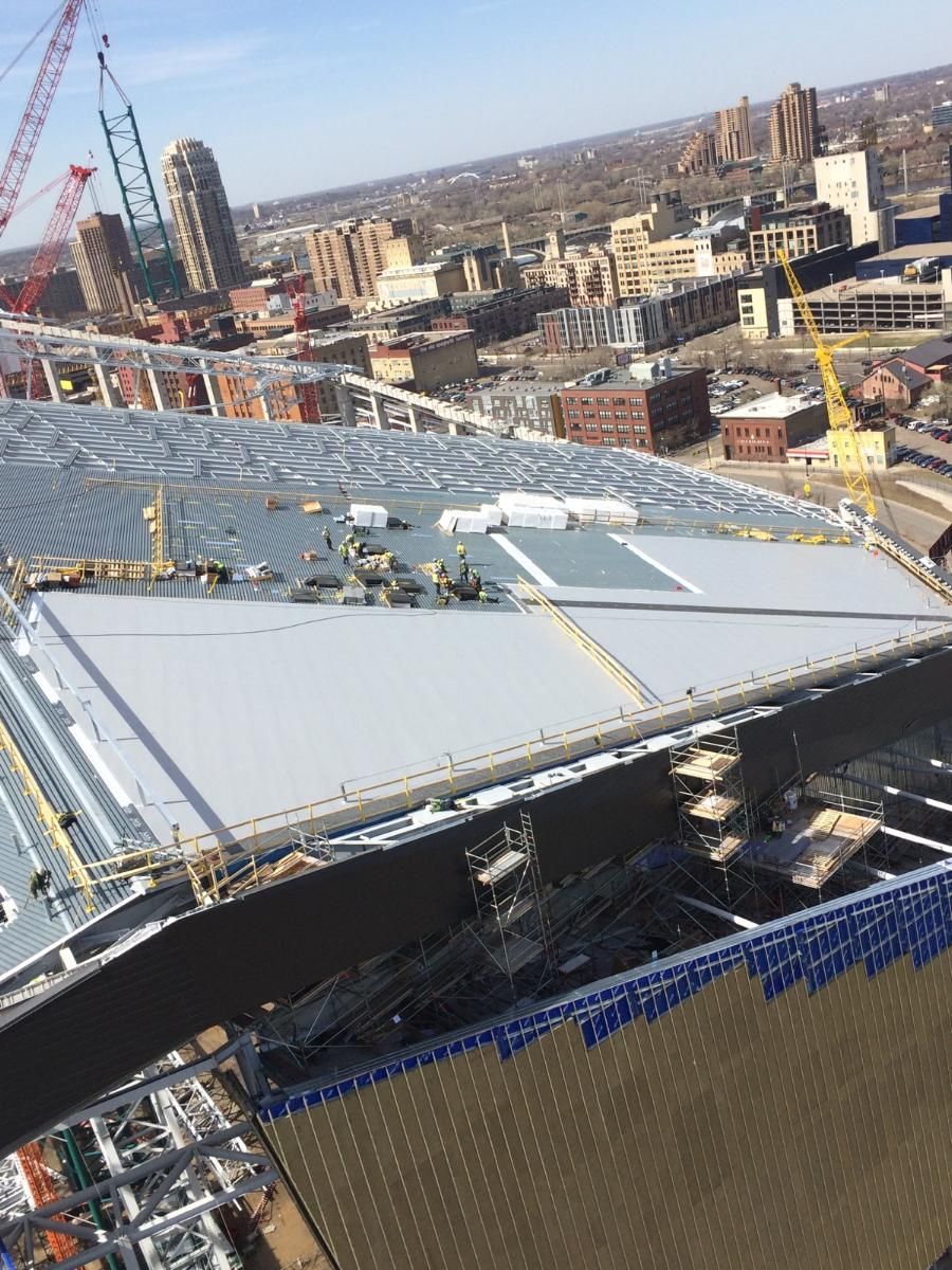 Construction site with cranes and a large, partially-built roof, in a cityscape setting.