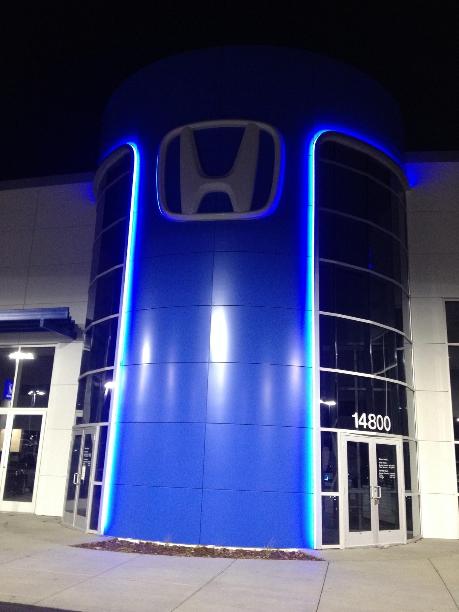 Night view of a Honda dealership with blue-lit exterior and illuminated logo.