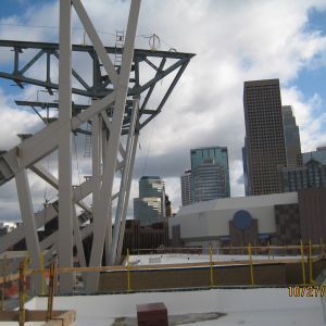 Construction site with steel framework against a cityscape and cloudy sky.