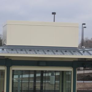 Off-white box on a building roof with a dark antenna, glass windows, and a green trim.