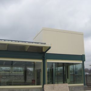 Modern building with large glass windows, teal accents, and beige upper walls under a cloudy sky.