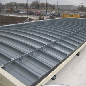 Curved metal roof with horizontal gray panels, sitting atop a white structure. Parking lot in the background.