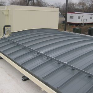 Curved, corrugated metal roof on a light-colored building with a neutral-toned box on top.