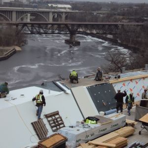 Construction workers on a roof overlooking a river and bridges.
