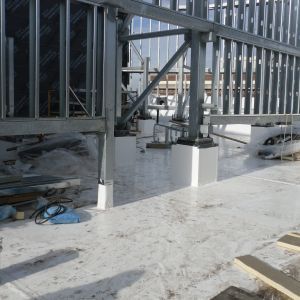 Construction site with metal framing on a white surface, supporting a structure against a background of buildings.