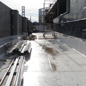 Construction site: building roof with metal sheeting, materials, and workers in the distance.