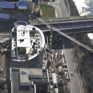 Construction site with a tall circular building, crane, and bridge.