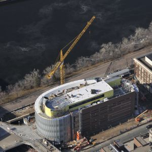 Construction site with yellow crane next to curved, modern building near a body of water.