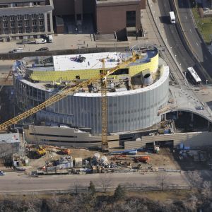 Construction site with a cylindrical, modern building. A crane is present.