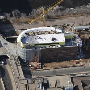 Construction site with partially built curved building, crane, and surrounding street.