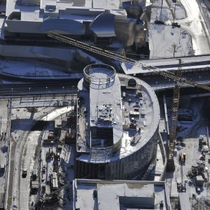 High-angle view of a building under construction, covered in snow with a crane, rail tracks, and surrounding buildings.