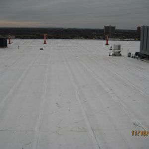 White commercial roof with orange cones and distant skyline under overcast sky.