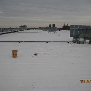 A flat, white rooftop with various mechanical equipment and a bucket. Cloudy sky overhead.