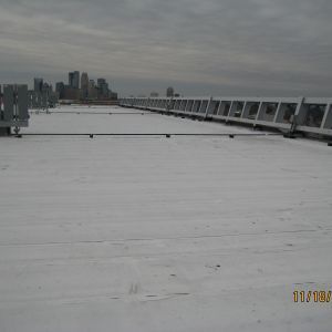 Flat white rooftop with metal structures, cityscape in the distance under overcast sky.
