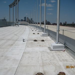 View of a flat, white roof with multiple silver poles in a row, cityscape visible in the background.