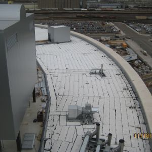 A rooftop with a white surface and industrial equipment. Buildings and a road are visible in the background.