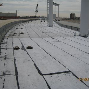 Flat roof with light-colored surface, several black vent caps and vertical white columns.