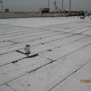 Flat commercial roof with white panels, a metal pipe, and construction equipment in the background.