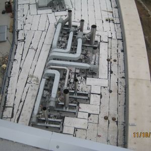 Overhead view of a roof with vent pipes and cracked white panels.