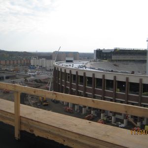 Construction site with a partially built, circular brick building; wooden railing in foreground.