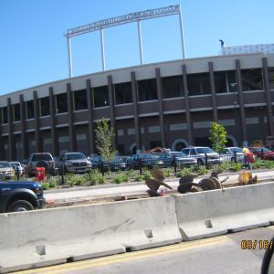 Stadium exterior with cars parked in front and construction barriers.