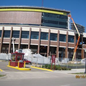 Stadium under construction with brick facade and glass windows; an orange lift is visible.