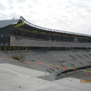 Stadium under construction with exposed metal, concrete seating, and safety tape.