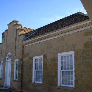 Stone building with white-framed windows and door under a brown roof, against a clear blue sky.