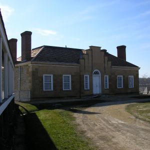 Tan, one-story building with white-framed windows, a central white door, and two chimneys under a blue sky.
