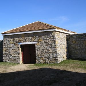 Stone building with red double doors, brown roof, and surrounding stone wall.