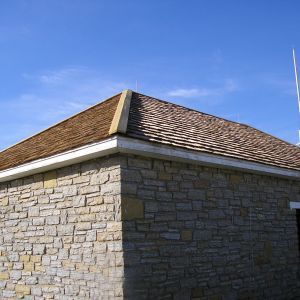 Stone building with brown shingle roof against a blue sky.