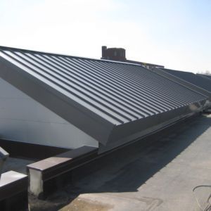 Gray metal roof with ridges on a white building, sunny outdoors.